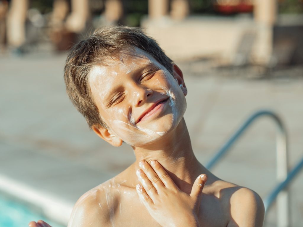 A Child smiles with closed eyes. It has sunscreen all over his face 